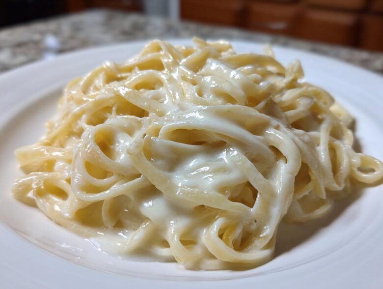 Close-up of fettuccine pasta generously coated in rich, creamy homemade alfredo sauce on a white plate.