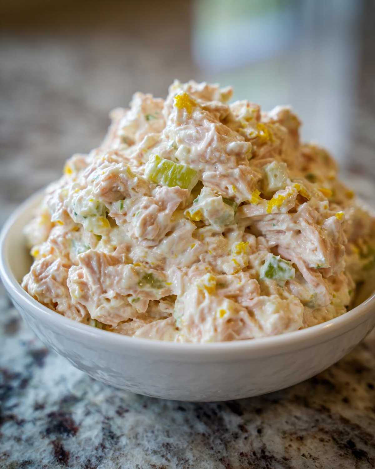 Close-up of a generous serving of creamy ham salad with visible chunks of ham, celery, and yellow zest in a white bowl.