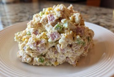 A generous scoop of creamy ham salad featuring diced ham, celery, and egg yolk served on a white plate.
