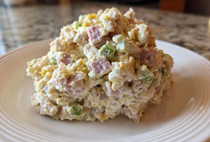 A generous scoop of creamy ham salad featuring diced ham, celery, and egg yolk served on a white plate.