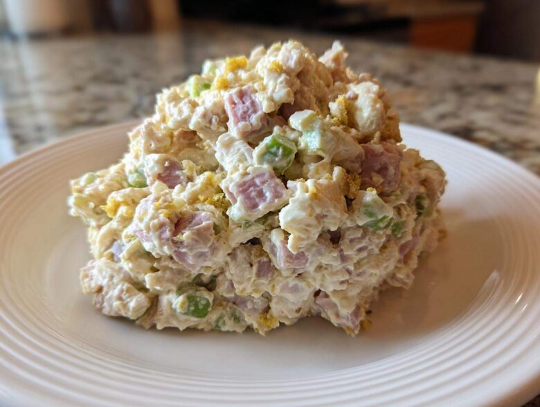 A generous scoop of creamy ham salad featuring diced ham, celery, and egg yolk served on a white plate.