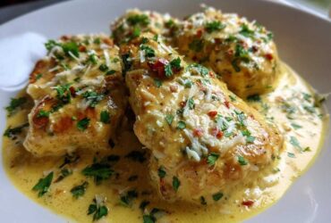 Close-up of three pieces of golden seared creamy lemon chicken smothered in a rich yellow sauce, garnished with Parmesan and parsley.