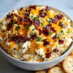 A close-up of creamy Million Dollar Dip loaded with shredded cheddar cheese, crispy bacon bits, and green onions.