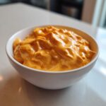 A small white bowl filled with thick, bright orange, creamy nacho cheese sauce.