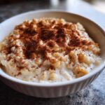 Close-up of creamy rice pudding served in a white bowl and generously sprinkled with cinnamon.