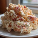 A mound of creamy seafood salad featuring shredded white and pink seafood mixed in a mayonnaise dressing, served on a white plate.