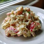 A mound of creamy seafood salad featuring chunks of pink seafood, mixed with dressing and topped with fresh dill.