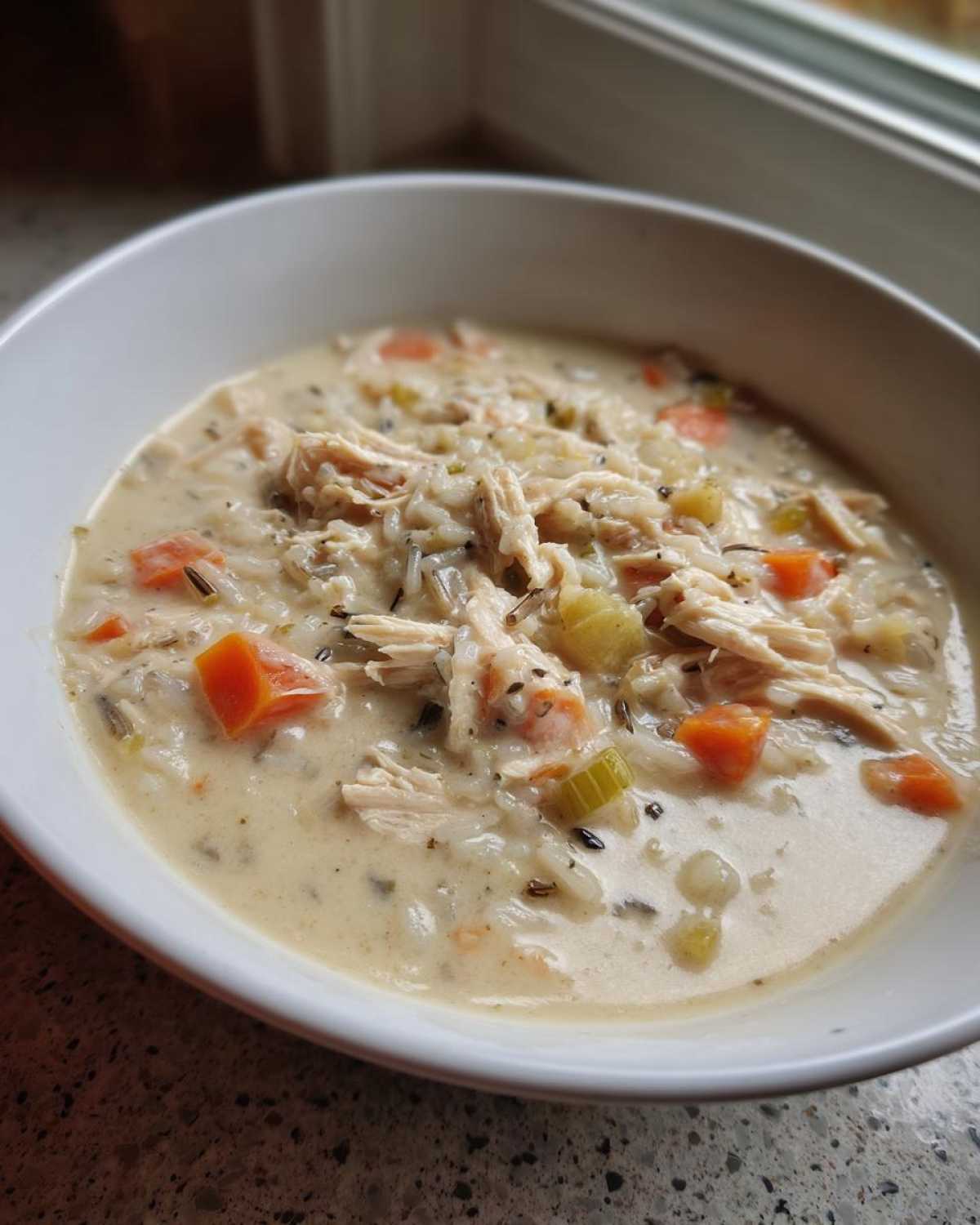 A close-up of a creamy bowl of amazing 6-ingredient wild rice soup, featuring shredded chicken, carrots, and celery.
