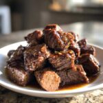 A pile of tender, saucy cubes of crockpot steak served on a white plate.