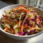 Close-up of a vibrant bowl filled with crunchy cabbage salad, featuring shredded green cabbage, purple cabbage, and carrots.