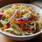 A vibrant close-up of crunchy cabbage salad featuring shredded green and purple cabbage, carrots, and red onion slices.