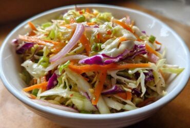 A vibrant close-up of crunchy cabbage salad featuring shredded green and purple cabbage, carrots, and red onion slices.