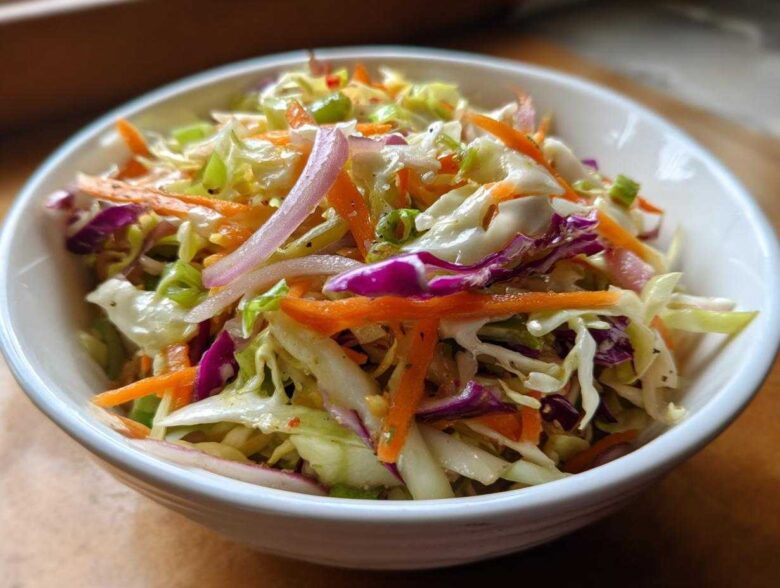 A vibrant close-up of crunchy cabbage salad featuring shredded green and purple cabbage, carrots, and red onion slices.