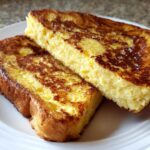 Two thick slices of golden brown easy french toast stacked slightly on a white plate.