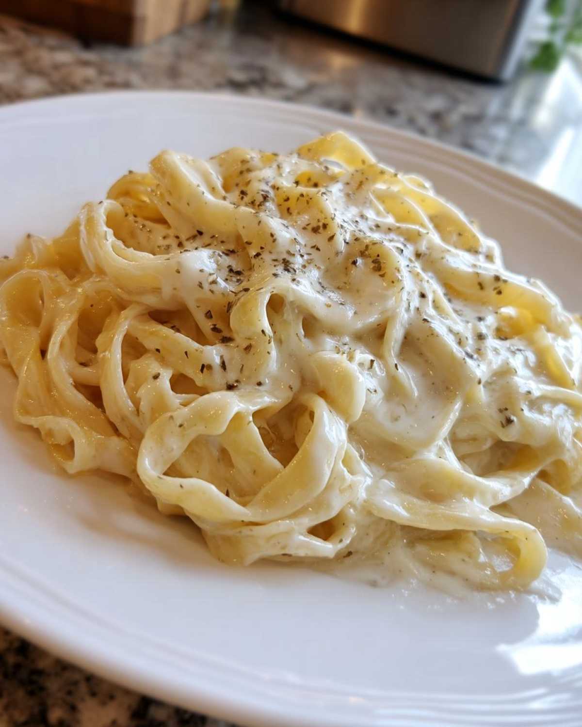 Close-up of fettuccine pasta generously coated in rich homemade alfredo sauce and sprinkled with herbs.