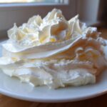 A beautiful swirl of fluffy, white cream cheese frosting piped onto a small white plate.