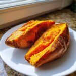 Two fluffy baked sweet potato halves seasoned with salt and pepper on a white plate.