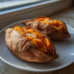 Two fluffy baked sweet potatoes, split open and topped with coarse sea salt, sitting on a white plate.