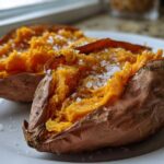 Two fluffy baked sweet potatoes split open and topped with coarse sea salt flakes.