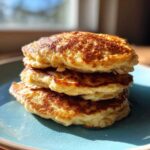 A close-up stack of three fluffy, golden-brown banana pancakes served on a blue plate.