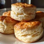 A stack of freshly baked, golden-brown buttermilk biscuits showing flaky layers.