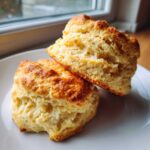 Two tall, fluffy homemade scones stacked slightly on a white plate, showing their flaky texture.