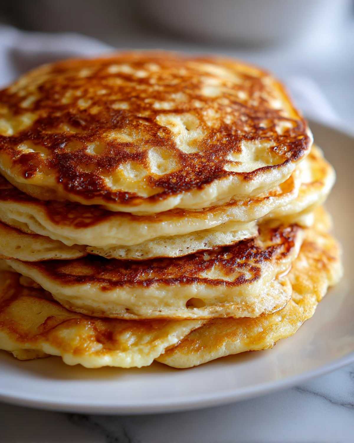 A tall stack of golden brown, fluffy sourdough pancakes piled high on a white plate.