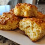 Close-up of several tall, golden brown homemade scones stacked on a white plate, showing a fluffy interior.