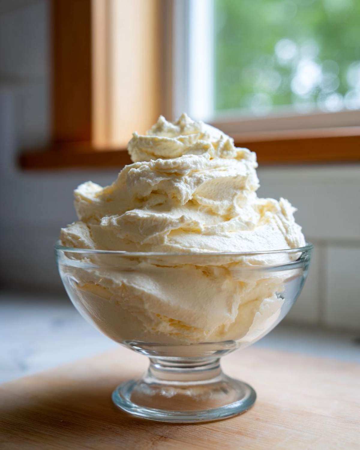 A generous serving of fluffy vanilla buttercream frosting piped high in a clear glass dessert dish.