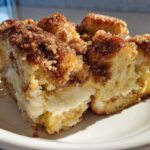 A close-up of a square serving of french toast casserole with a visible layer of cream cheese filling.