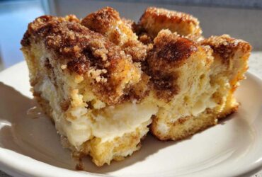 A close-up of a square serving of french toast casserole with a visible layer of cream cheese filling.