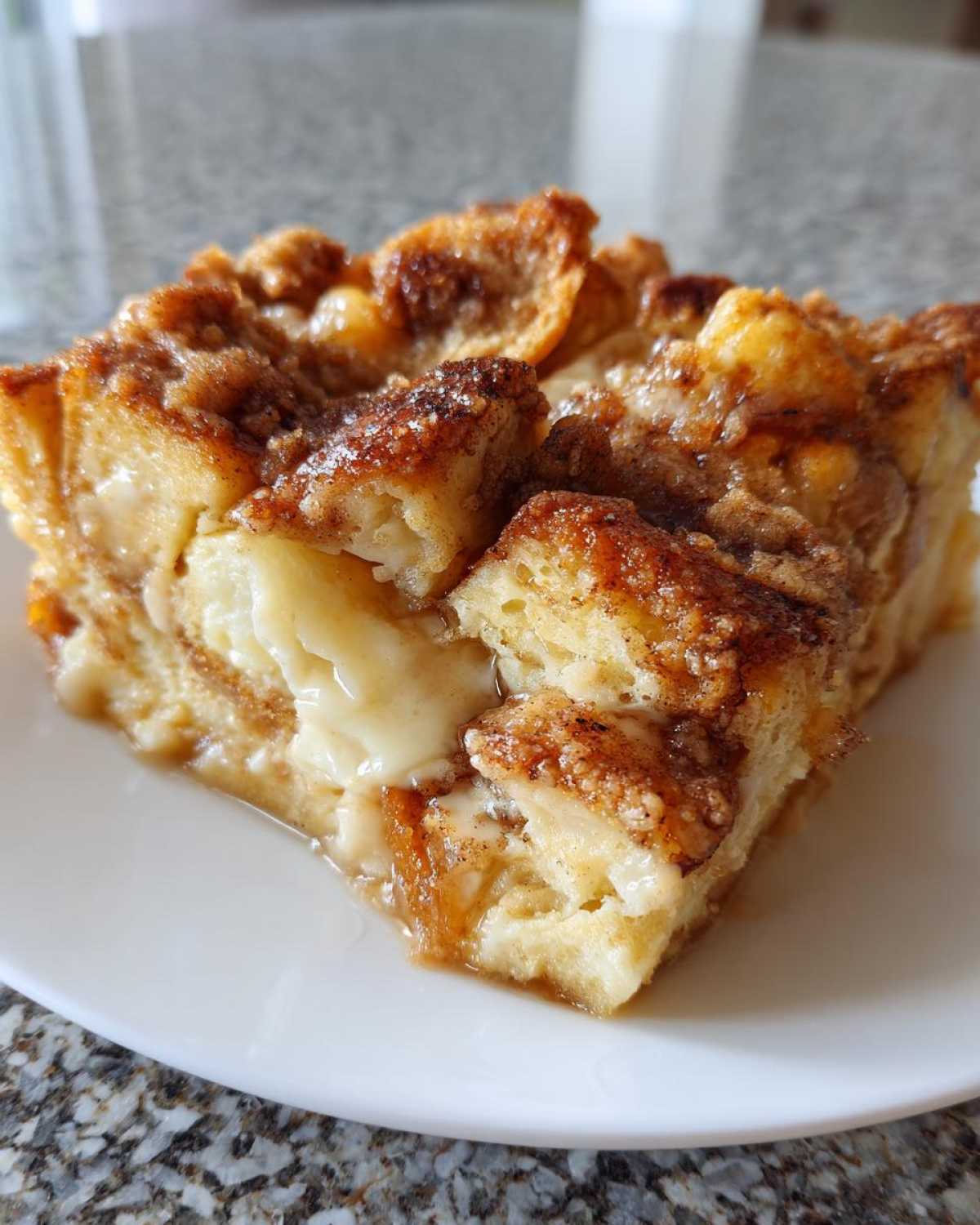A moist, square slice of baked french toast casserole with a caramelized, cinnamon-sugar topping, served on a white plate.