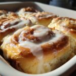 Close-up of several warm, freshly baked cinnamon roll swirls topped with thick white icing.
