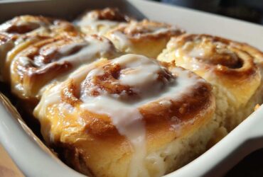 Close-up of several warm, freshly baked cinnamon roll swirls topped with thick white icing.
