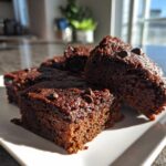 Close-up of several fudgy sweet potato brownies topped with chocolate chips, served on a white plate.