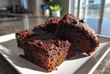 Close-up of several fudgy sweet potato brownies topped with chocolate chips, served on a white plate.