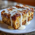 A rich, golden-brown slice of bread pudding drizzled generously with white vanilla glaze.