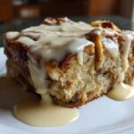 A close-up of a square slice of moist bread pudding topped generously with a thick vanilla cream sauce.