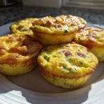Five freshly baked, golden brown Egg Muffin Cups with visible ham and chives on a white plate.
