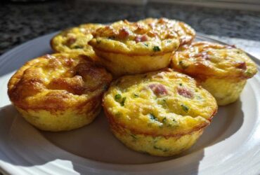Five freshly baked, golden brown Egg Muffin Cups with visible ham and chives on a white plate.