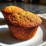 Close-up of a perfectly baked, golden brown honey bran muffin sitting on a white plate.