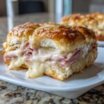 Close-up of a gooey Ham and Cheese Sliders piece showing melted cheese oozing out with ham slices inside a toasted bun.