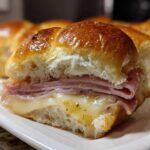 A close-up view of a freshly baked Ham and Cheese Sliders, showing melted cheese and layers of ham inside a shiny, golden bun.