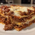 A close-up of a hearty, layered slice of homemade lasagna featuring rich meat sauce and melted white cheese.