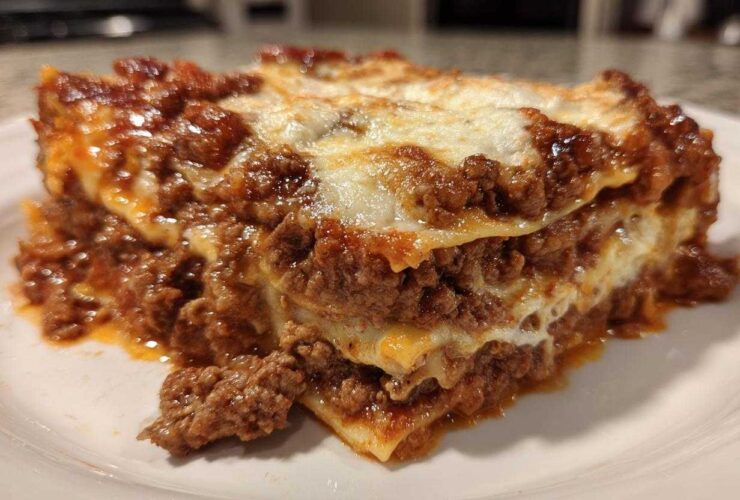 A close-up of a hearty, layered slice of homemade lasagna featuring rich meat sauce and melted white cheese.