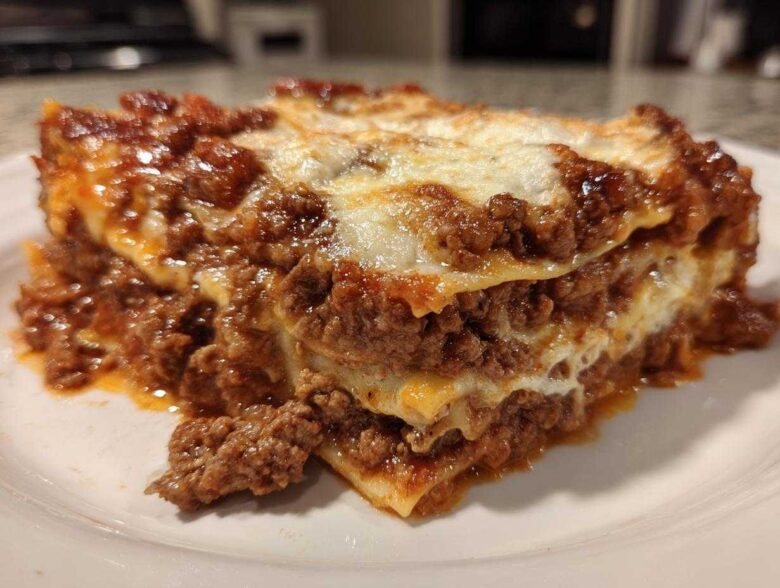 A close-up of a hearty, layered slice of homemade lasagna featuring rich meat sauce and melted white cheese.