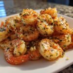 A pile of perfectly cooked, seasoned air fryer shrimp dusted with garlic and parsley on a white plate.