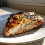 Cross-section of a juicy Greek chicken breast showing the white meat and herb marinade.