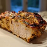 Close-up of a perfectly cooked, juicy piece of greek chicken, showing the white interior and charred, herbed exterior.