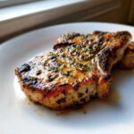 Close-up of a perfectly cooked, juicy pork chop coated in a savory herb marinade for pork chops.